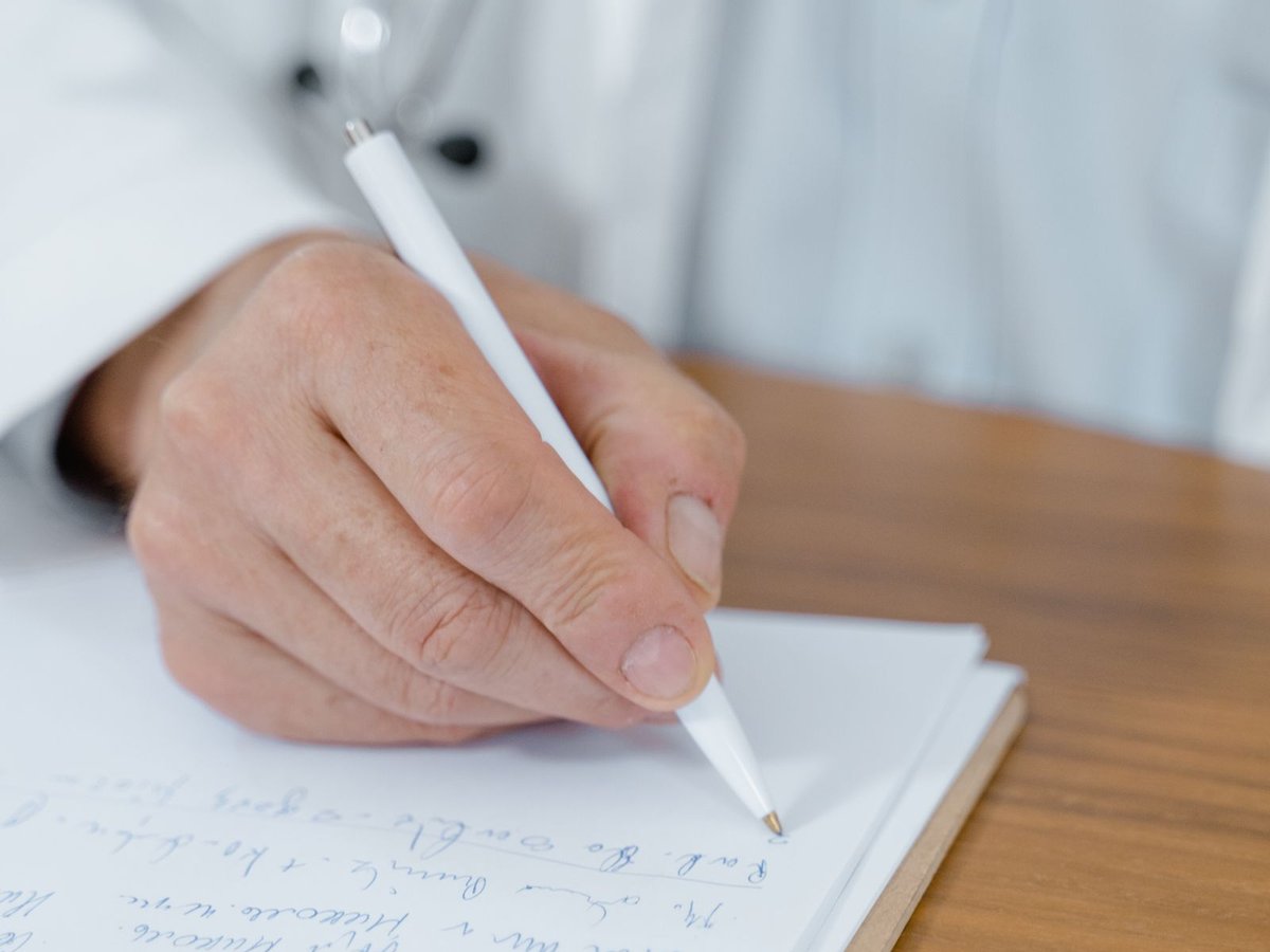 Doctor's hands recording a skin assessment plan on a clinical notepad, part of the doctor-led triage used at Rejuvena Bedford