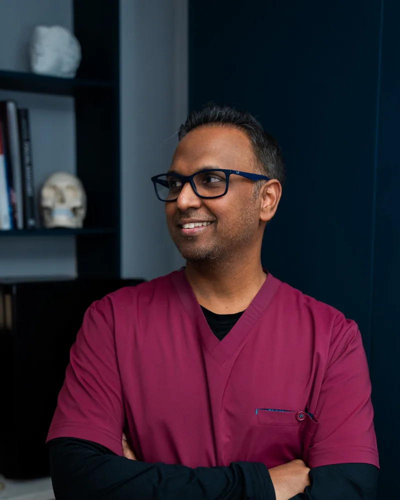 Dr Nick in his clinic room at Rejuvena Bedford, with dermatology reference books and anatomy models behind him