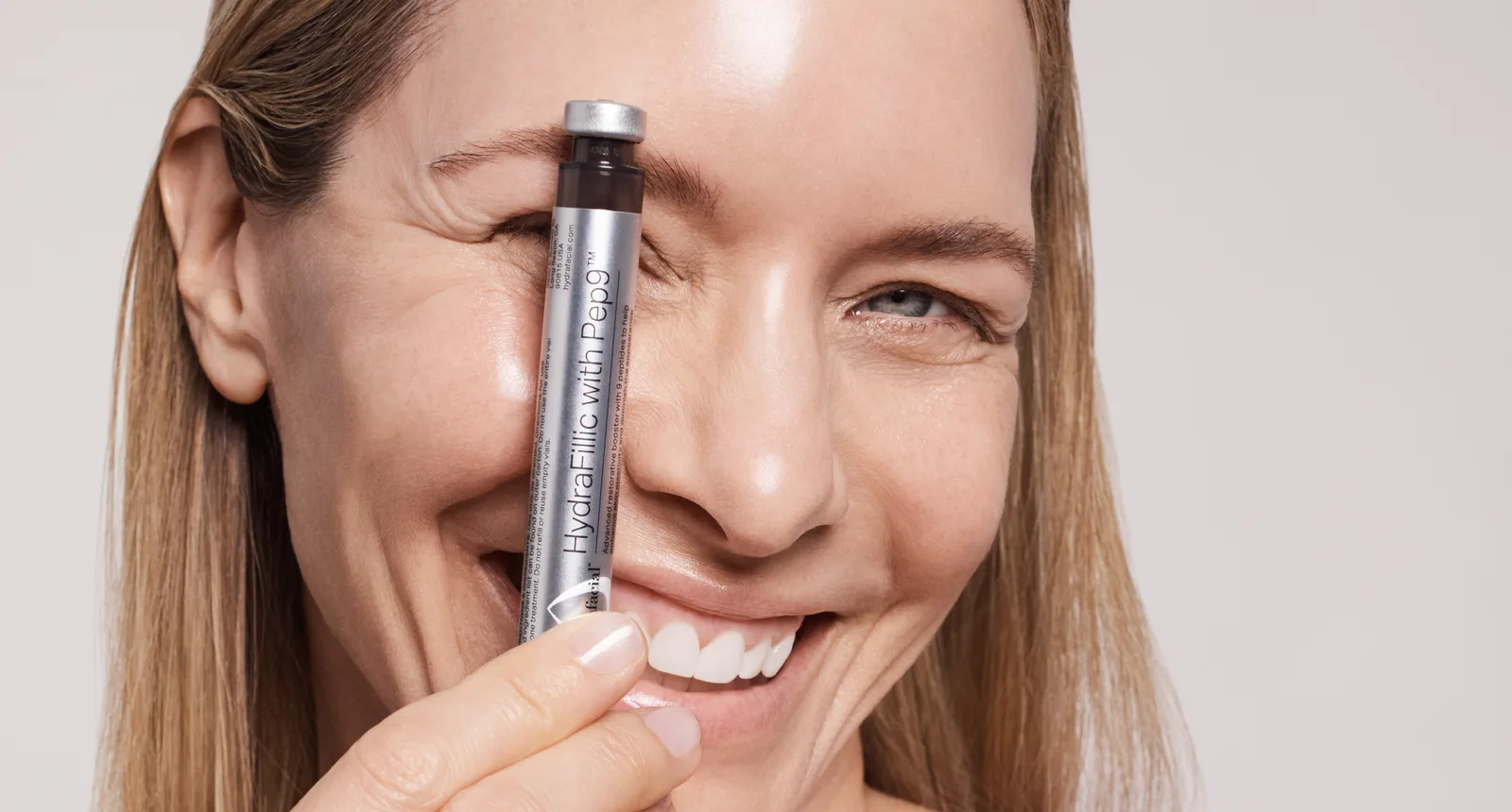 Smiling model holding a HydraFacial serum vial (official HydraFacial image)