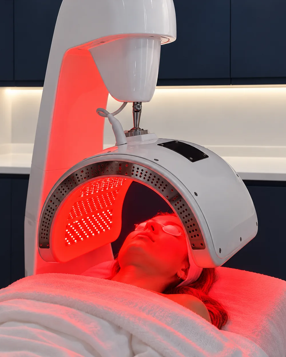 A client lying under the glowing red Dermalux&reg; Triwave LED canopy at Rejuvena Clinic, Bedford